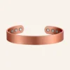 Jonc ouvert en cuivre rosé à surface lisse, avec quatre pastilles rondes claires à l'intérieur de chaque extrémité